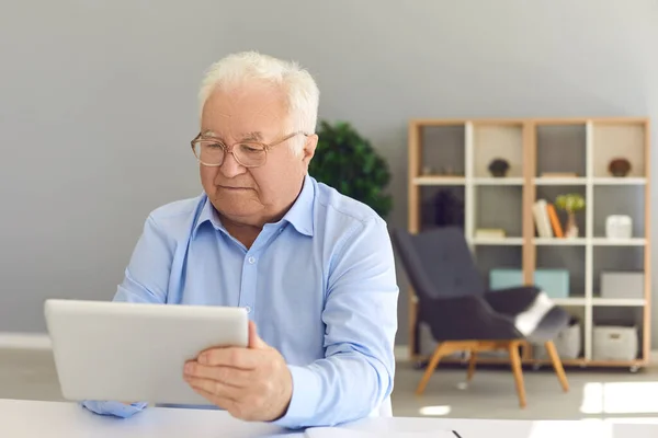 Ανώτερος άνδρας που χρησιμοποιεί tablet για να κλείσετε ραντεβού με γιατρό, να ελέγξετε το συνταξιοδοτικό πρόγραμμα ή να διαβάσετε ειδήσεις — Φωτογραφία Αρχείου