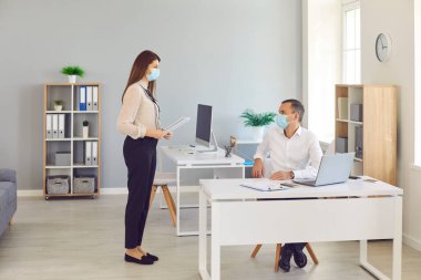 Koruyucu maskeler takan ofis çalışanları ofiste iletişim kurarken güvenlik mesafesine bağlı kalırlar..