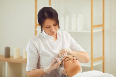 Kadın dermatolog, kadınların alnına yaşlanma önleyici botoks iğnesi yapıyor.