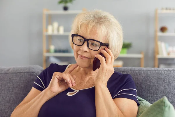 Femme mûre pensive parlant à des parents sur un téléphone portable assis sur le canapé à la maison — Photo