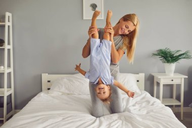 Mutlu genç anne hafta sonu evde eğleniyor ve küçük oğluyla rahat bir yatakta oynuyor.