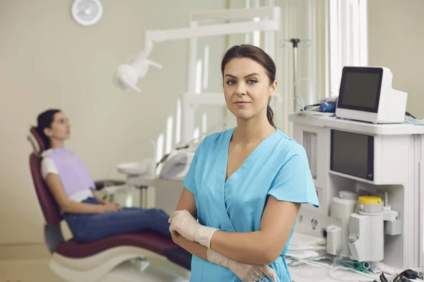 Dentist looking at camera with sitting woman patient at background — Stock Photo, Image