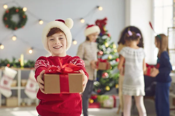 Porträt eines niedlichen lächelnden Jungen, der ein Weihnachtsgeschenk in den Händen hält und es im Wohnzimmer verschenkt. — Stockfoto