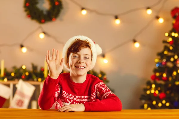 Щасливий хлопчик посміхається і махає рукою, кажучи привіт під час відеодзвінка або різдвяного прямого ефіру — стокове фото