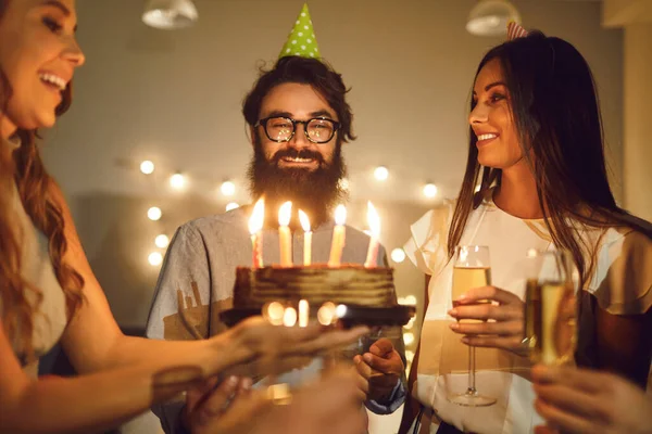 Young women wishing Happy Birthday to their friend and giving him cake with burning candles