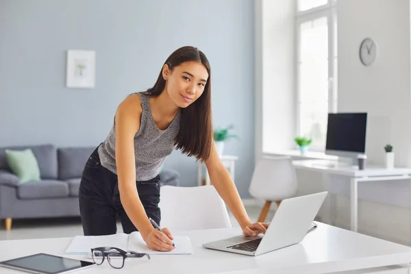 Junge Frau mit Laptop und Notizbuch, die ihren Tag plant, fernarbeitet oder studiert — Stockfoto