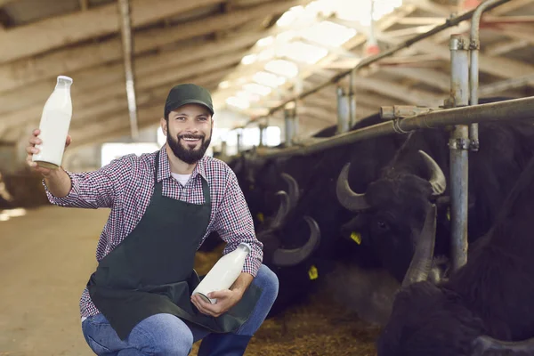 Gelukkige boer toont flessen verse natuurlijke buffelmelk vervaardigd op zijn boerderij — Stockfoto