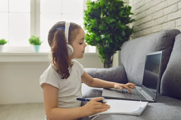 Školačka ve sluchátkách dává lekci sledování videohovoru na virtuálního učitele laptopu doma. — Stock fotografie