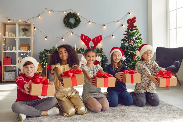 Bir grup mutlu çocuk yerde oturuyor ve ellerinde Noel hediyeleri var. — Stok fotoğraf