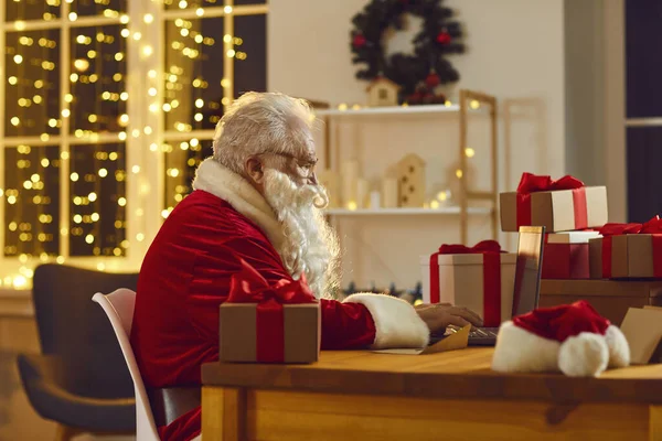 Santa Claus working on his laptop, answering emails and ordering presents delivery online — Stock Photo, Image