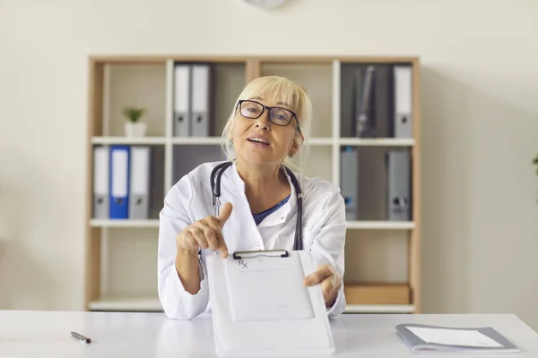 Médico senta-se na frente da câmera e mostra uma receita para seu paciente usando uma chamada de vídeo. — Fotografia de Stock