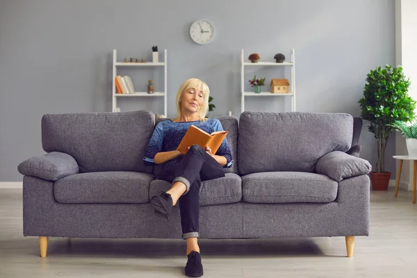 Ritratto di una donna anziana concentrata seduta su un divano e che legge un libro interessante. — Foto Stock