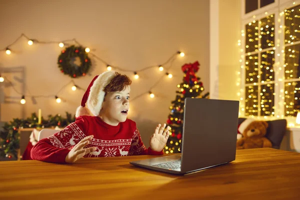 Šokovaný dítě sedí u stolu s notebookem při pohledu na skutečný Santa Claus na video chat — Stock fotografie