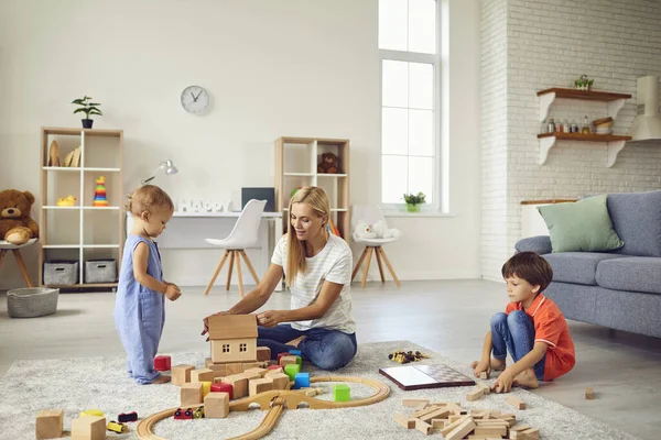 Matka gra w gry edukacyjne z uśmiechniętymi dziećmi na podłodze w domu — Zdjęcie stockowe