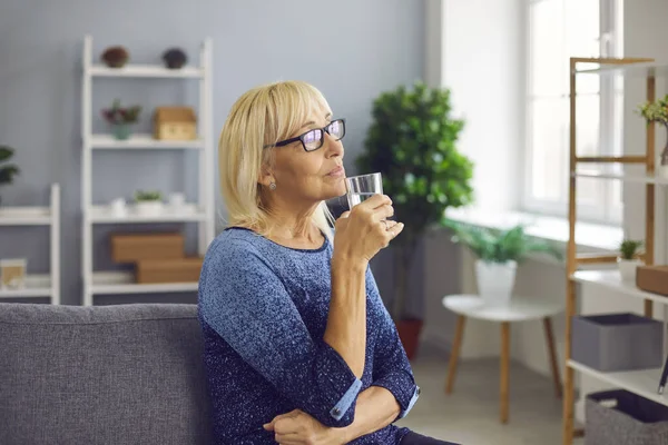 Düşünceli yaşlı kadın susuz ve sağlıklı kalmak için bir bardak saf temiz su içiyor. — Stok fotoğraf
