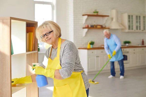 快乐的老年男女夫妇，穿着围裙和手套，在家里打扫卫生 — 图库照片
