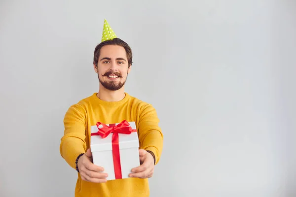 Young smiling man in festive clown hat showing holiday present box during videocall — Stock Photo, Image