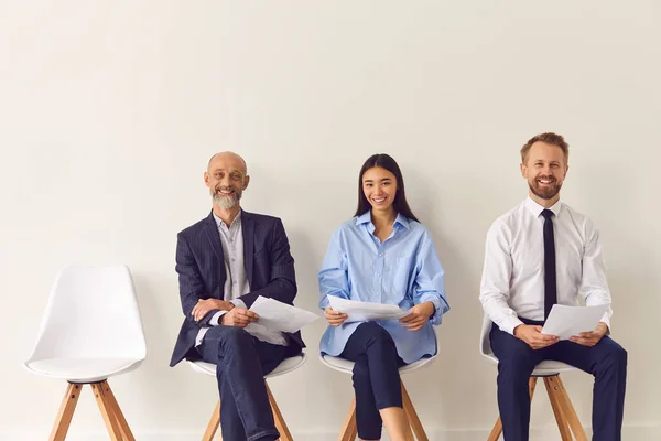 Três candidatos positivos de diferentes idades sentados em cadeiras à espera de entrevista de emprego — Fotografia de Stock