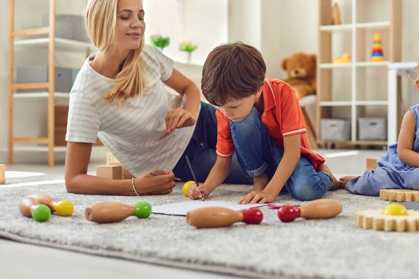 Mother sitting on floor carpet with children and drawing together at home — Stock Photo, Image