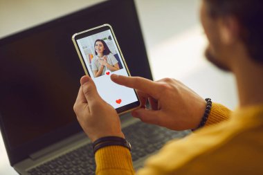 Bekar bir adam flört uygulamasında güzel genç kadınların fotoğraflarına bakıyor ve düğmeye basıyor.