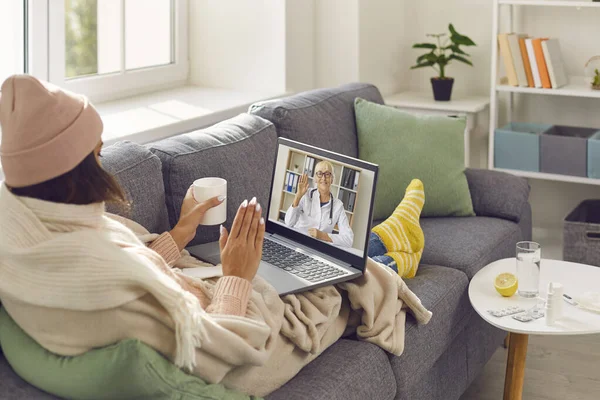 Chorą kobietę siedzącą na kanapie i wideo wzywającą lekarza e-zdrowia na konsultacje medyczne online — Zdjęcie stockowe