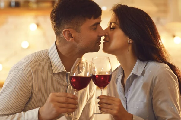 Jovem casal amoroso beijando uns aos outros e segurando copos de vinho durante a celebração do dia dos namorados — Fotografia de Stock