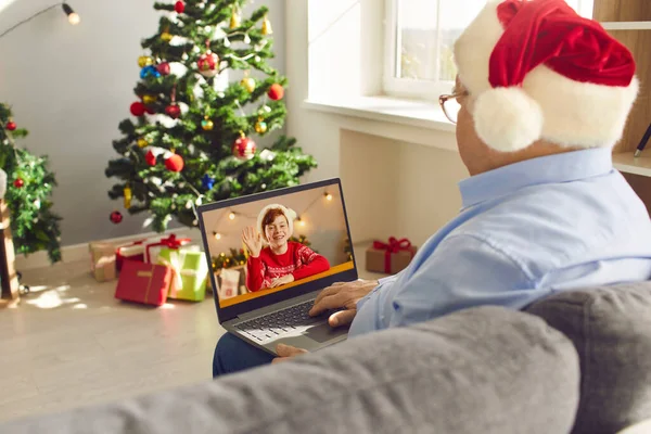 Granddad in Santa hat sitting on sofa at home on Christmas Day and video-calling his grandson — Stock Photo, Image