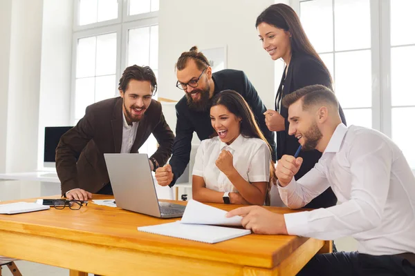 Team of excited colleagues looking at laptop screen celebrating successful sales