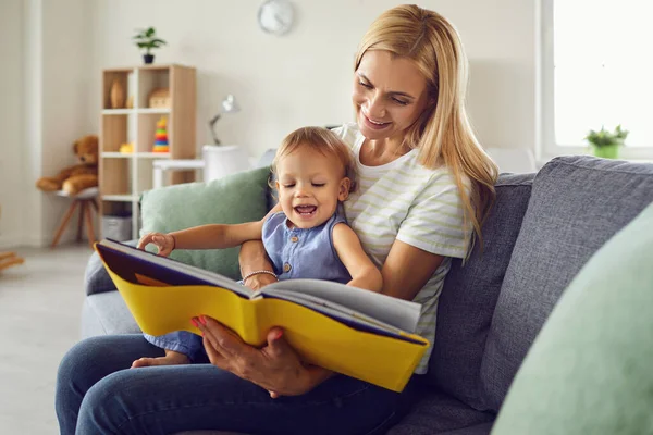 Happy mother with smiling baby on knees and reading book at home