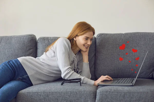 Gelukkig jong vrouw liggend op de bank met laptop, video bellen haar vriendje of chatten online — Stockfoto