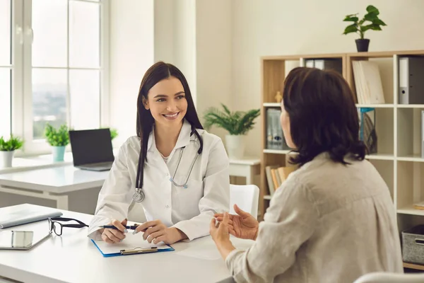 Giovane medico terapista sorridente che ascolta le lamentele dei pazienti nella clinica medica — Foto Stock