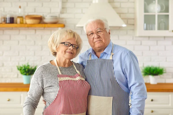 Ritratto di una coppia felice felice in grembiuli in cucina che abbraccia e guarda la macchina fotografica. — Foto Stock