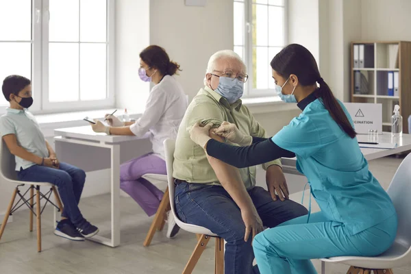Врач и медсестра в медицинской форме и защитных масках делают вакцинацию против вируса ковид-19 — стоковое фото