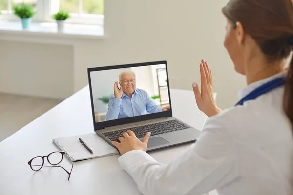 Усміхнений старший чоловік пацієнт привітання професійної жінки-лікар онлайн під час віддаленої зустрічі — стокове фото