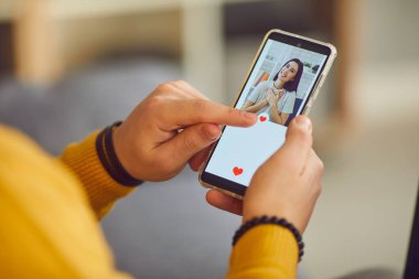 Adam kadın profillerini incelemek için akıllı telefon kullanıyor ve parmağıyla kalp düğmesine basıyor..