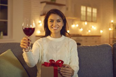 Online Sevgililer Günü 'nde elinde şarap ve bayram hediyesi tutan mutlu bir kadın.