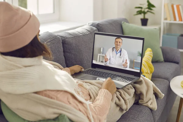 Sıcak ekose kumaşlara sarılı hasta kadın kanepede oturup video aracılığıyla çevrimiçi doktorla konuşuyor. — Stok fotoğraf