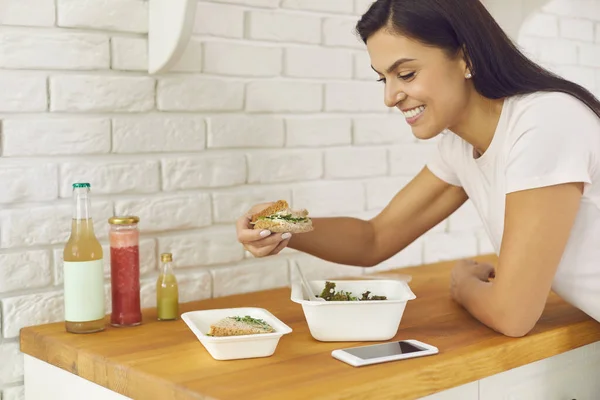 Jovem feliz desfrutando saudável takeaway salada vegetal e sanduíche em casa — Fotografia de Stock