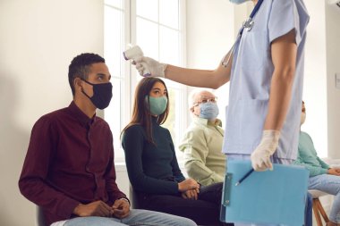 Temassız dijital termometre kullanarak hastaların vücut ısısını ölçen bir tıp çalışanı.