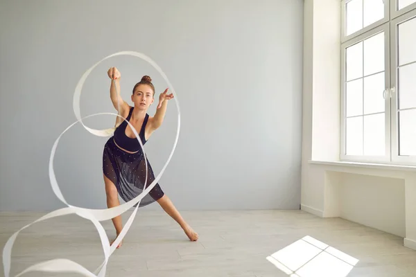 Młoda gimnastyczka rytmiczna ćwicząca ruchy z wstążką na ciepłym piętrze w nowoczesnym studio — Zdjęcie stockowe