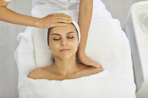 Mujer con los ojos cerrados se encuentra en un spa y recibe un masaje facial con las manos de un masajista. —  Fotos de Stock