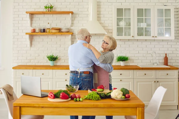 Felice coppia anziana abbracciare o ballare in cucina durante la cottura pasto vegano fresco sano — Foto Stock