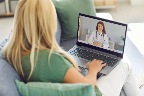 Nézet hátulról egy nő beszél egy videohívás közben az orvos ül a kanapén otthon. — Stock Fotó
