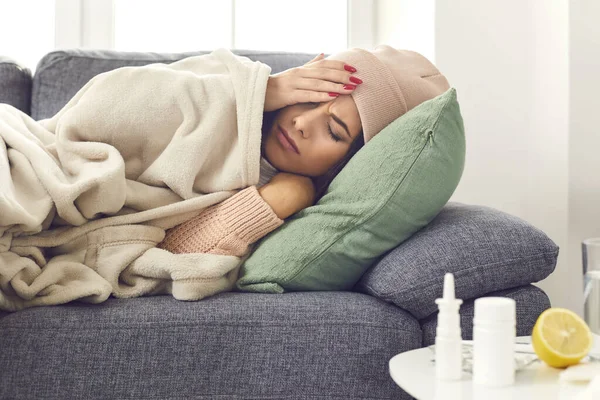 Close up of a sick woman with flu, fever and headache lying wrapped in a plaid on the couch. — Stock Photo, Image