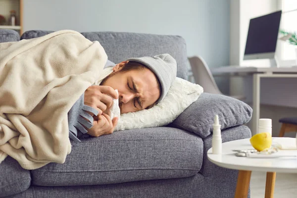 Primo piano di un uomo malato con un naso che cola con un tovagliolo tra le mani sdraiato sul divano. — Foto Stock