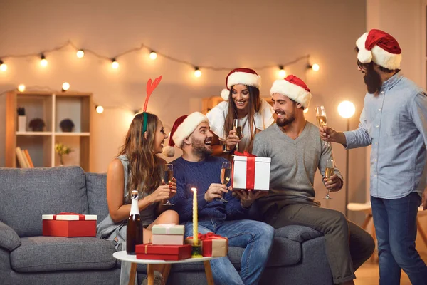 Felices amigos intercambiando regalos de Navidad y bebiendo champán en una pequeña fiesta en casa —  Fotos de Stock