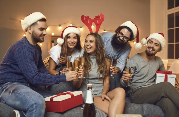 Grupa uśmiechniętych przyjaciół w czapkach wakacyjnych i akcesoriach ucztujących Boże Narodzenie z szampanem — Zdjęcie stockowe