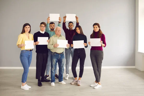 Grupp människor som står tillsammans, håller tomma pappersark och tittar på kameran — Stockfoto