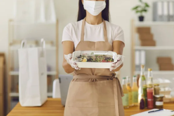 Afhaalcafé medewerker in medisch gezichtsmasker container met lunch klaar voor levering — Stockfoto