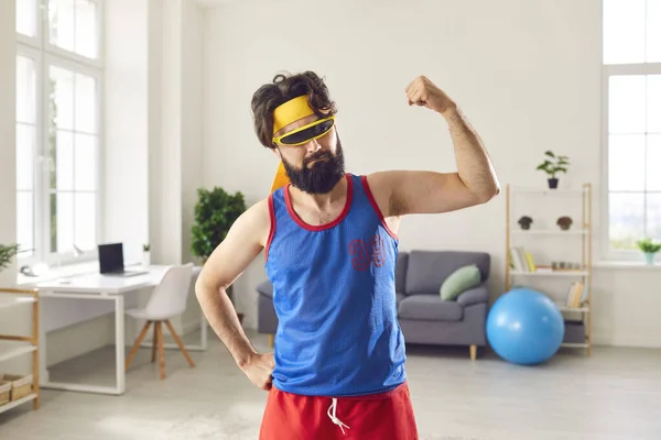 Смешной спортсмен хвастается своими худыми, слабыми мышцами рук после спортивных тренировок дома — стоковое фото